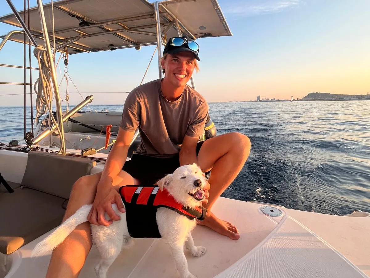 Lorenz en la popa de un catamarán navegando, con un perro con chaleco salvavidas